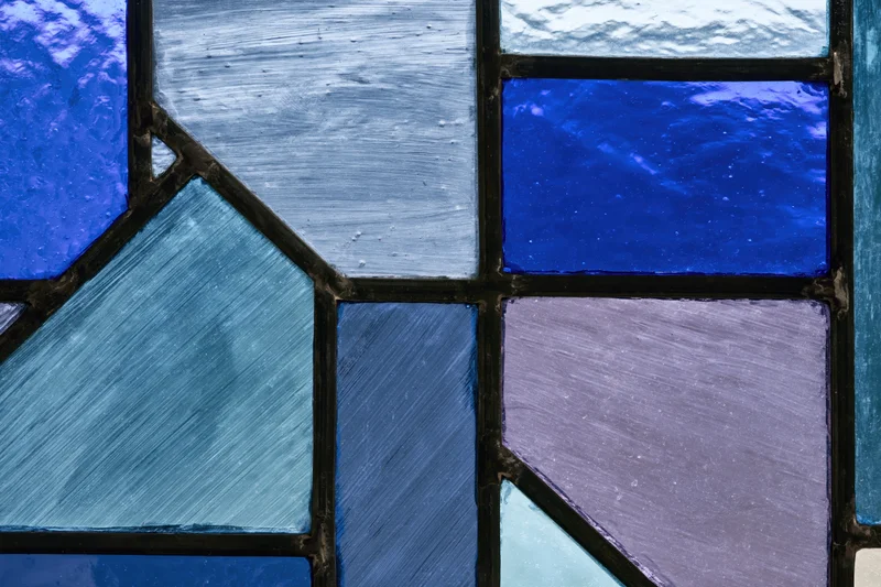 Close-up of a geometric stained glass window panel with blue and purple textured glass pieces arranged in a mosaic pattern