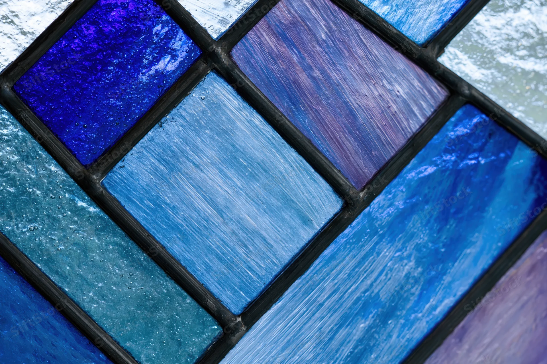 Close-up of a geometric stained glass window panel with blue and purple textured glass tiles arranged in a grid pattern