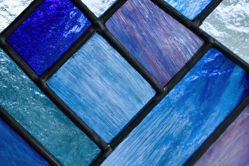 Close-up of a geometric stained glass window panel with blue and purple textured glass tiles arranged in a grid pattern