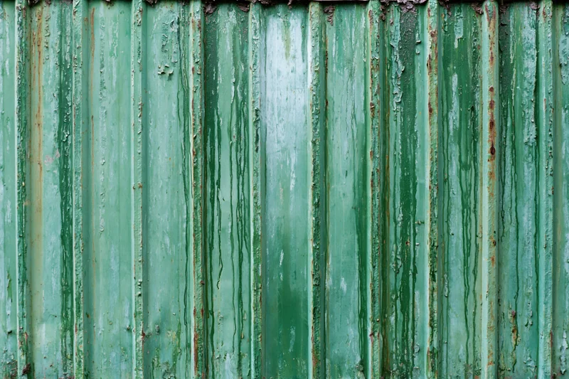Weathered green corrugated metal fence panel with peeling paint and rust streaks