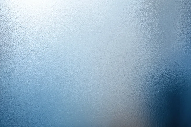 Frosted textured glass surface in close-up flat view with blue gradient and soft light diffusion