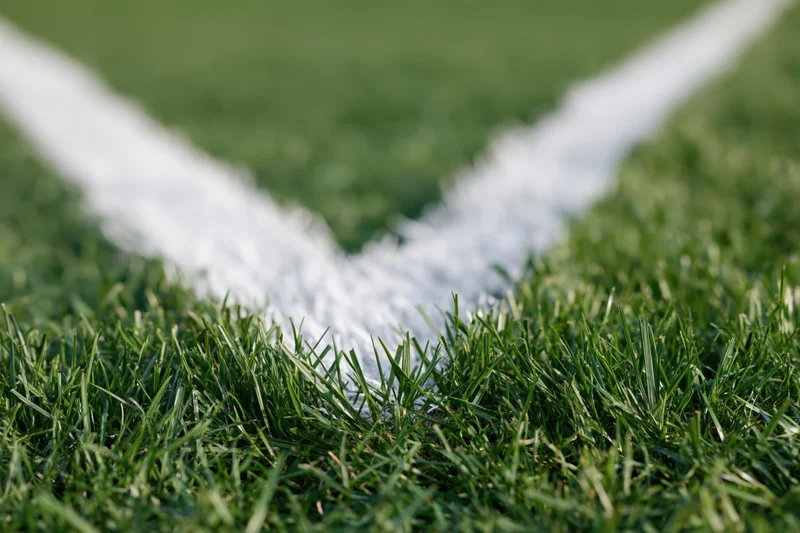 Close-up of white corner marking lines on green football pitch grass