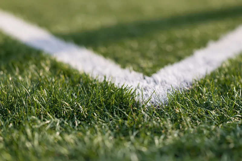 Close-up ground-level view of white corner marking lines on a green football pitch grass surface