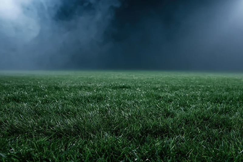 Close-up ground-level view of a professional football pitch under dark stormy sky