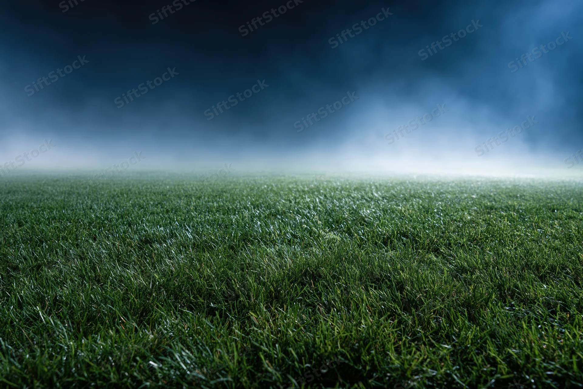 Close-up ground-level view of a professional football pitch under stormy sky