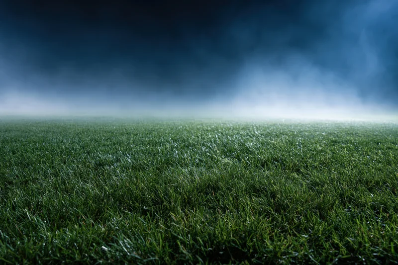Close-up ground-level view of a professional football pitch under stormy sky
