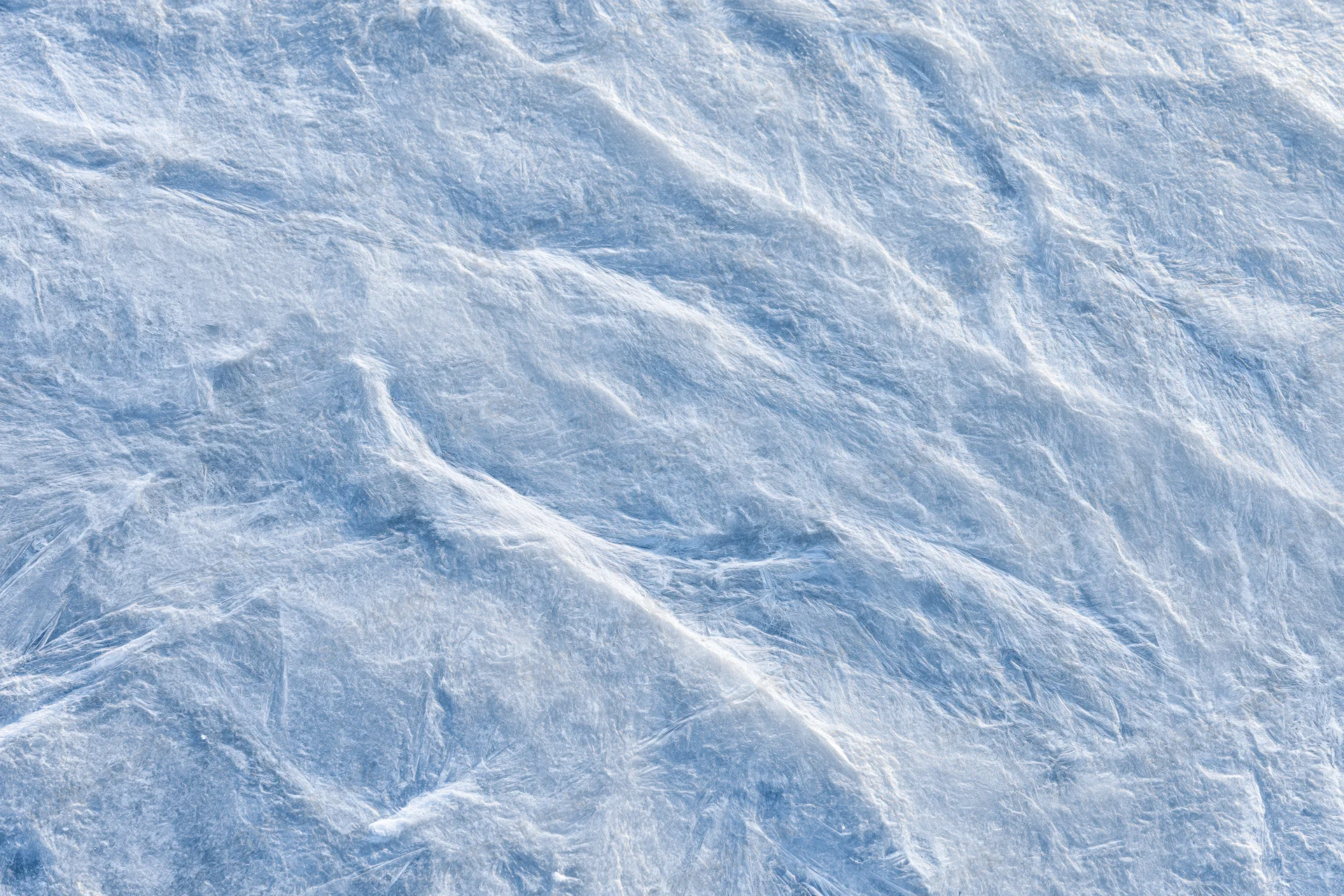 Close-up of a frozen ice surface showing intricate crystalline texture and subtle blue-white patterns
