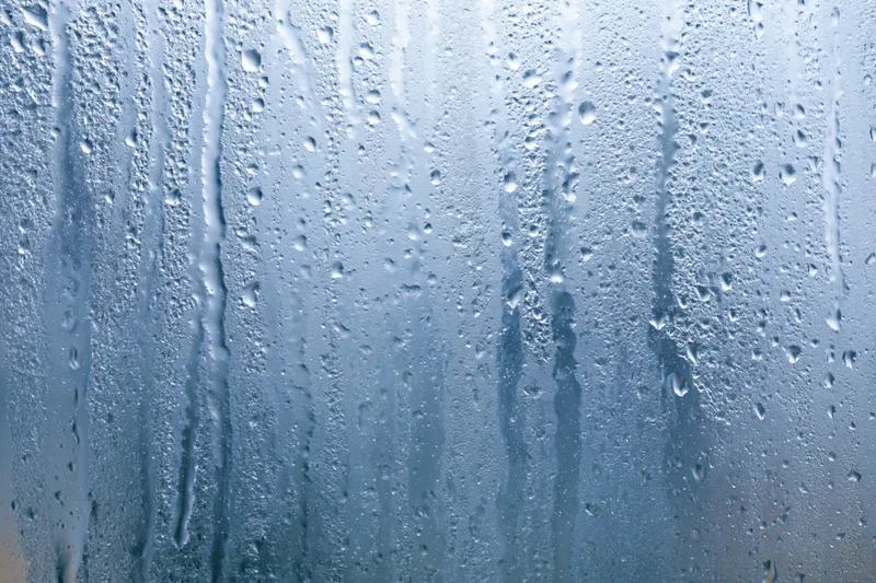 Wet glass window with rain droplets and streaks running vertically