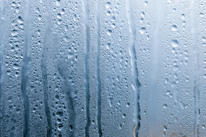 Wet glass window surface with water droplets and streaks from condensation