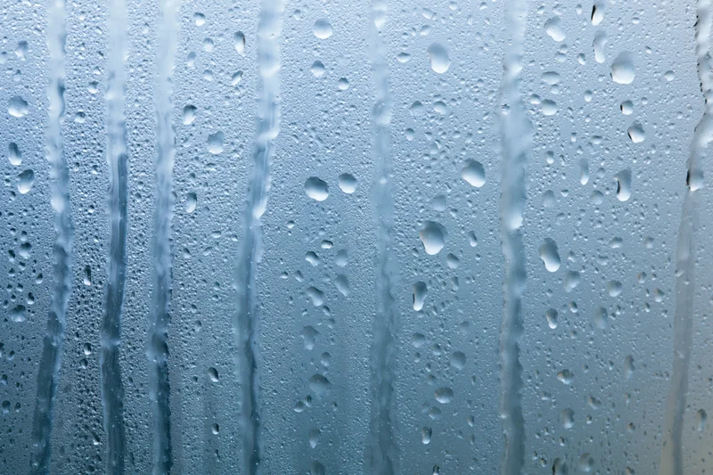 Wet glass window with rain droplets and vertical streaks from condensation