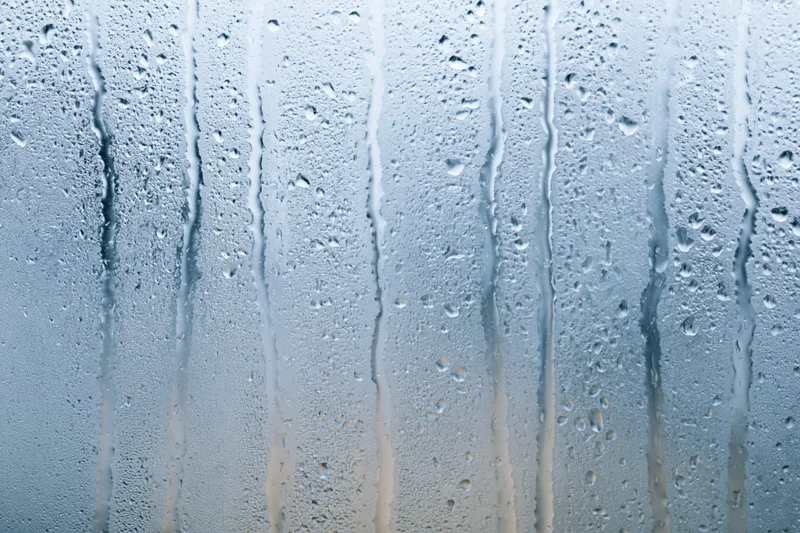 Wet glass window with rain droplets and vertical streaks from condensation