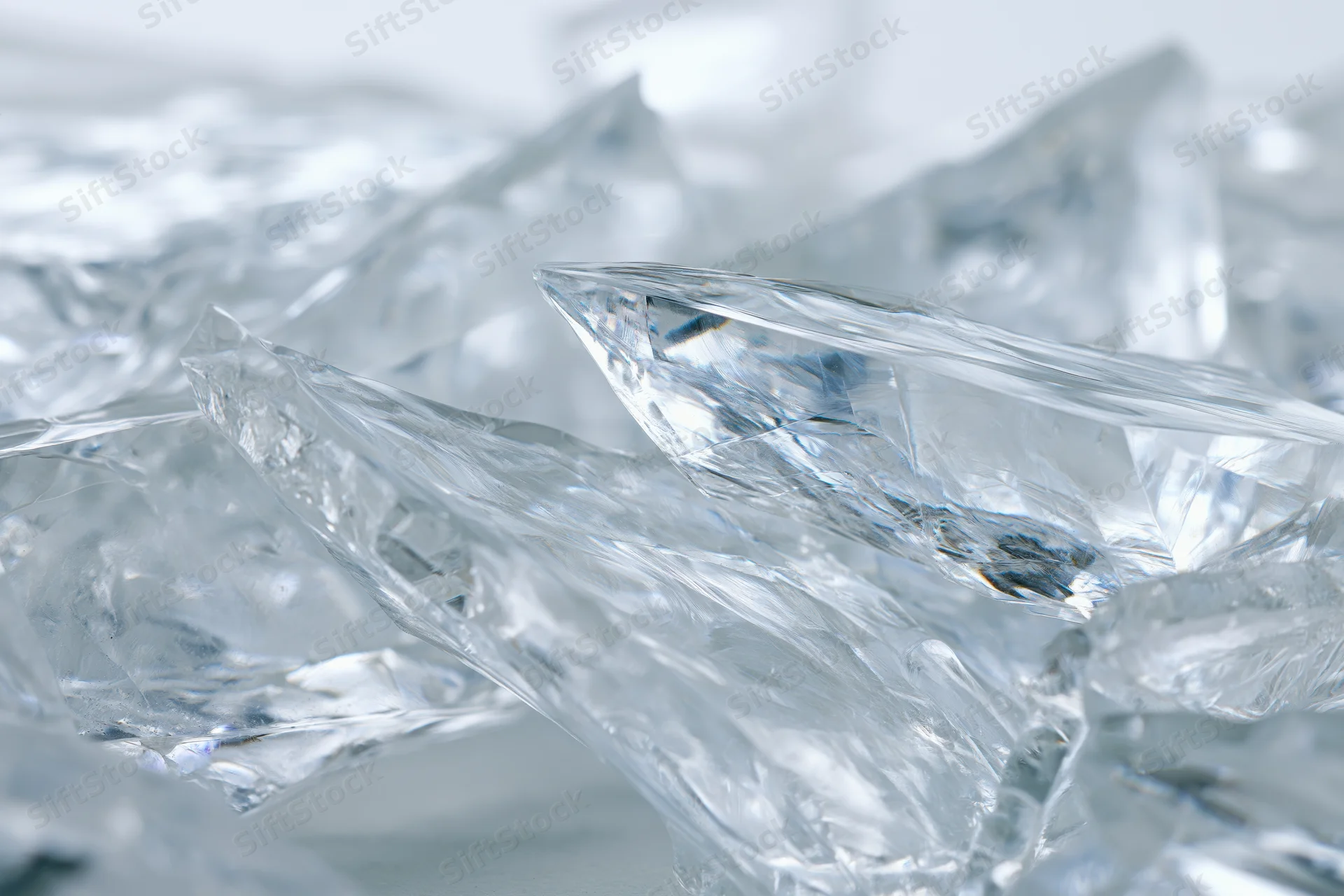 Close-up of fractured glass shards with sharp edges and transparent surfaces scattered in a pile