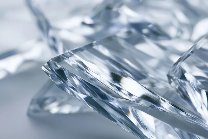 Fractured glass shard with sharp edges and light reflections on a smooth surface