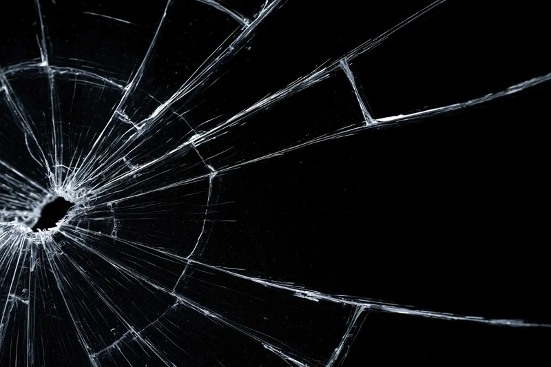 Shattered glass surface with radiating cracks against black background