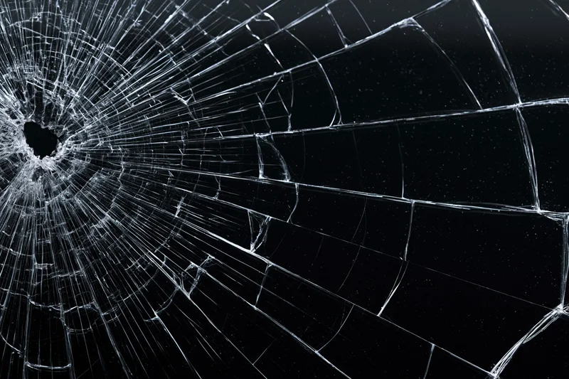 Shattered glass surface with radiating cracks from a central impact point against a dark background