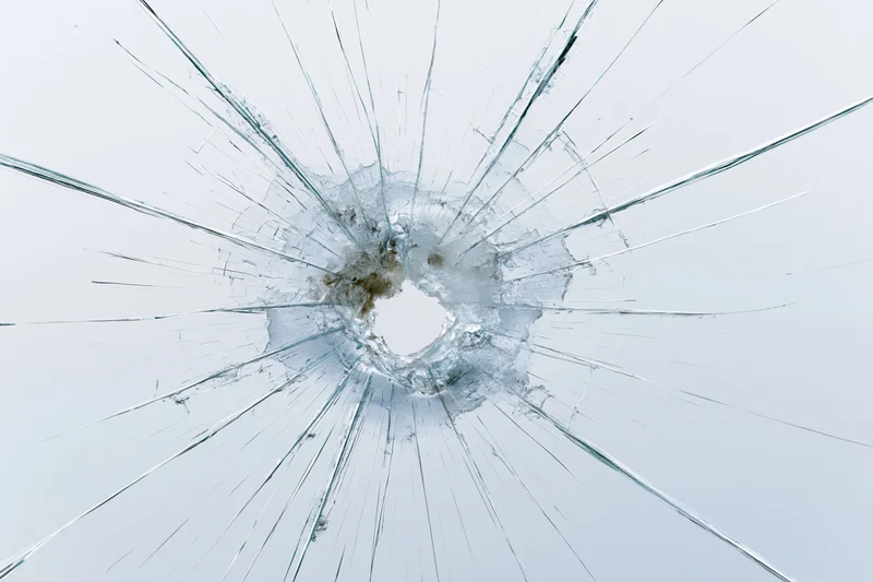 Shattered glass with radial cracks emanating from central impact hole