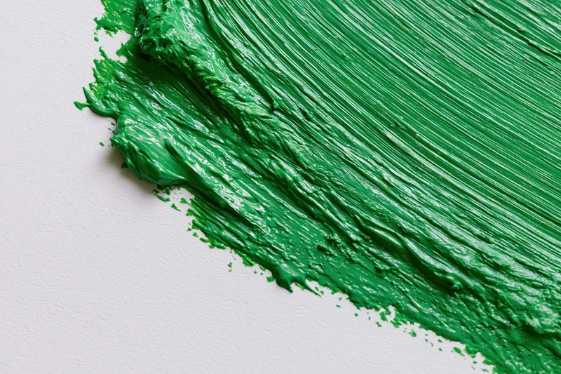 Thick green paint applied in diagonal brushstrokes on white surface