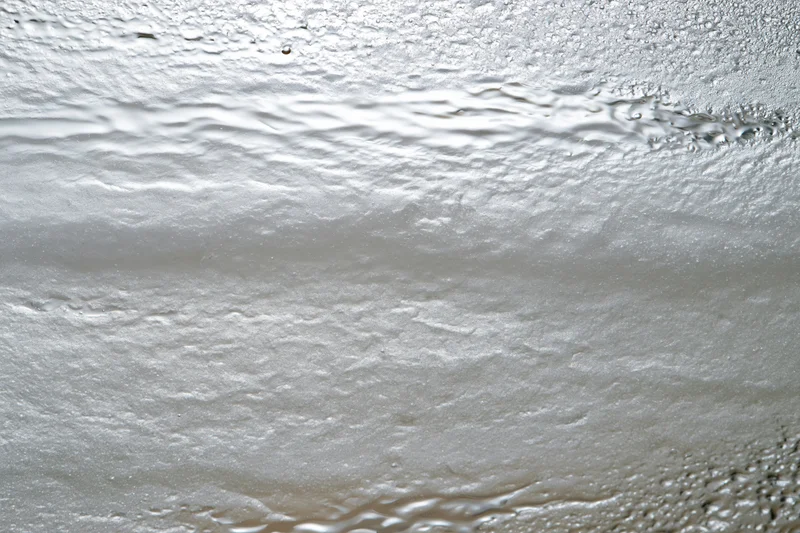 Wet glass surface covered in water droplets and condensation with visible ripples and texture