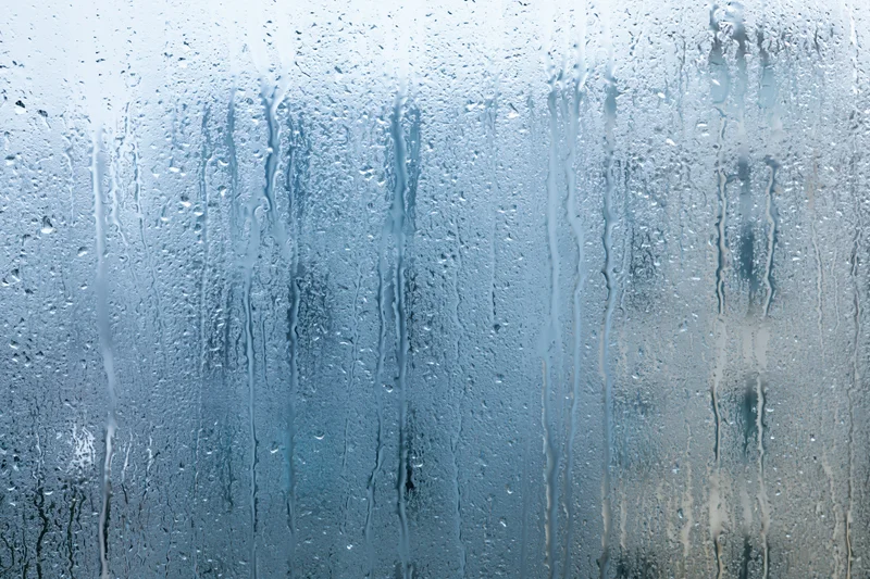 Rain-covered window glass with water droplets and streaks streaming down the surface