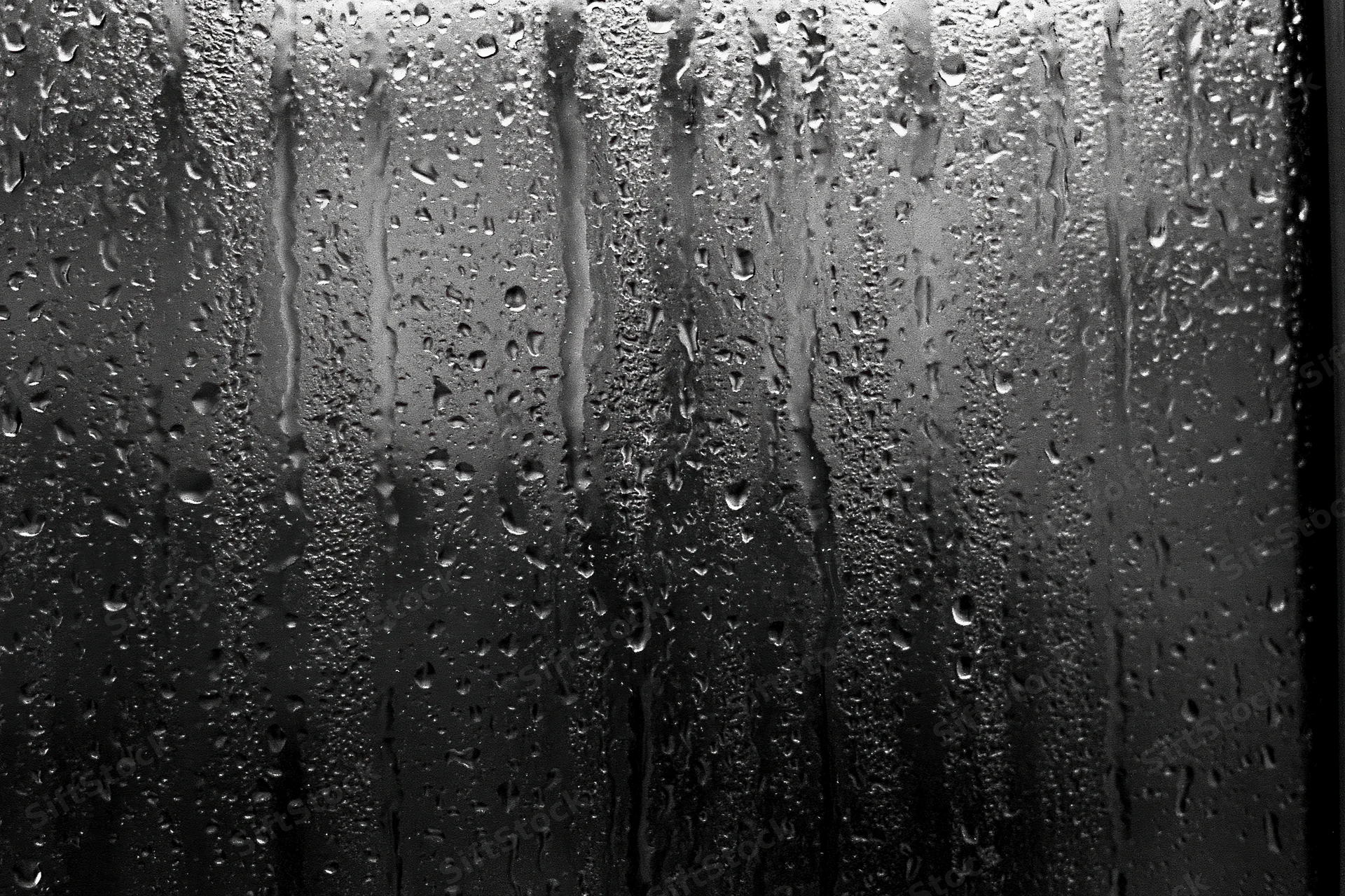 Rain-streaked dark glass window surface covered in water droplets and vertical streaks