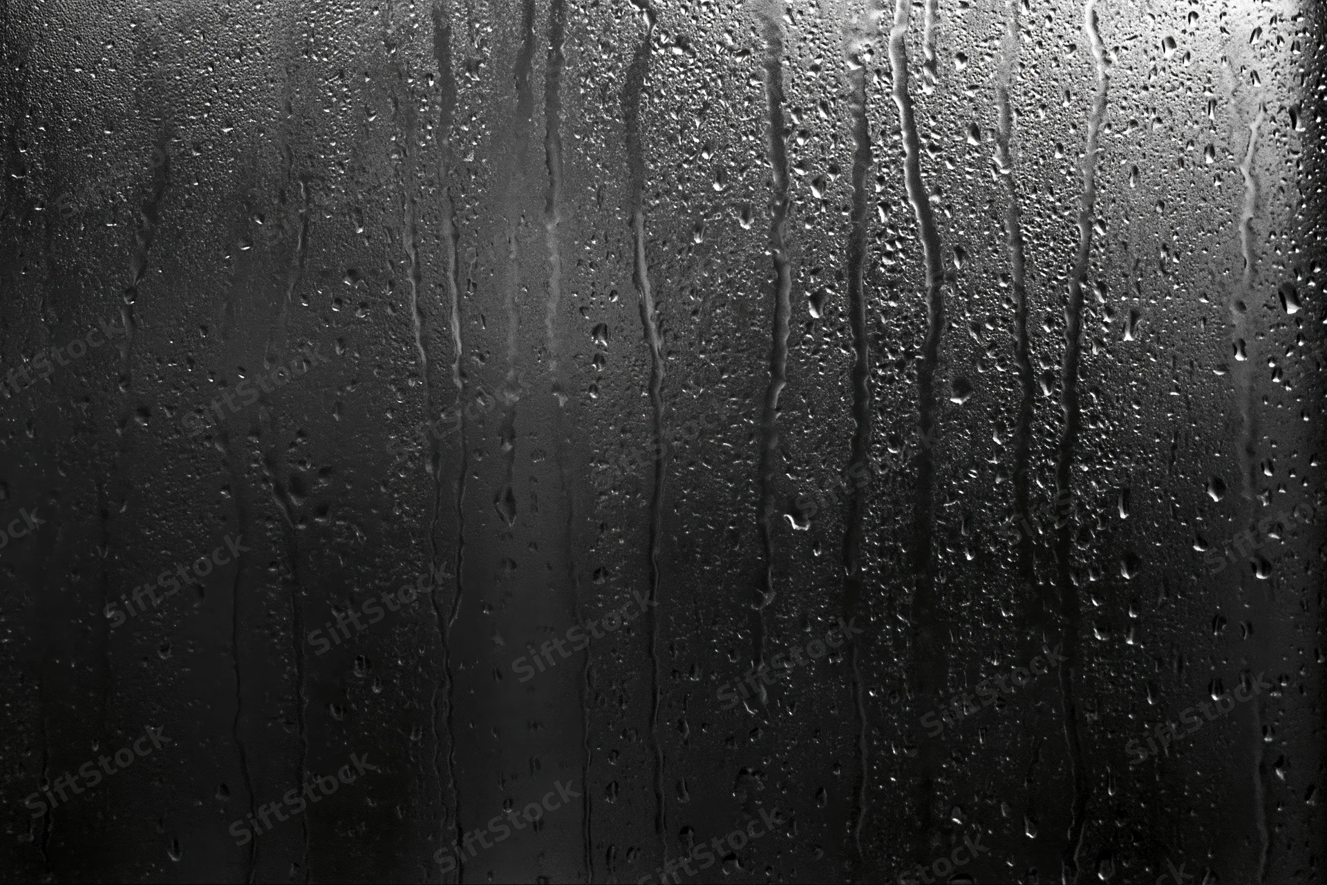 Rain-streaked dark glass window surface with water droplets and vertical streaks