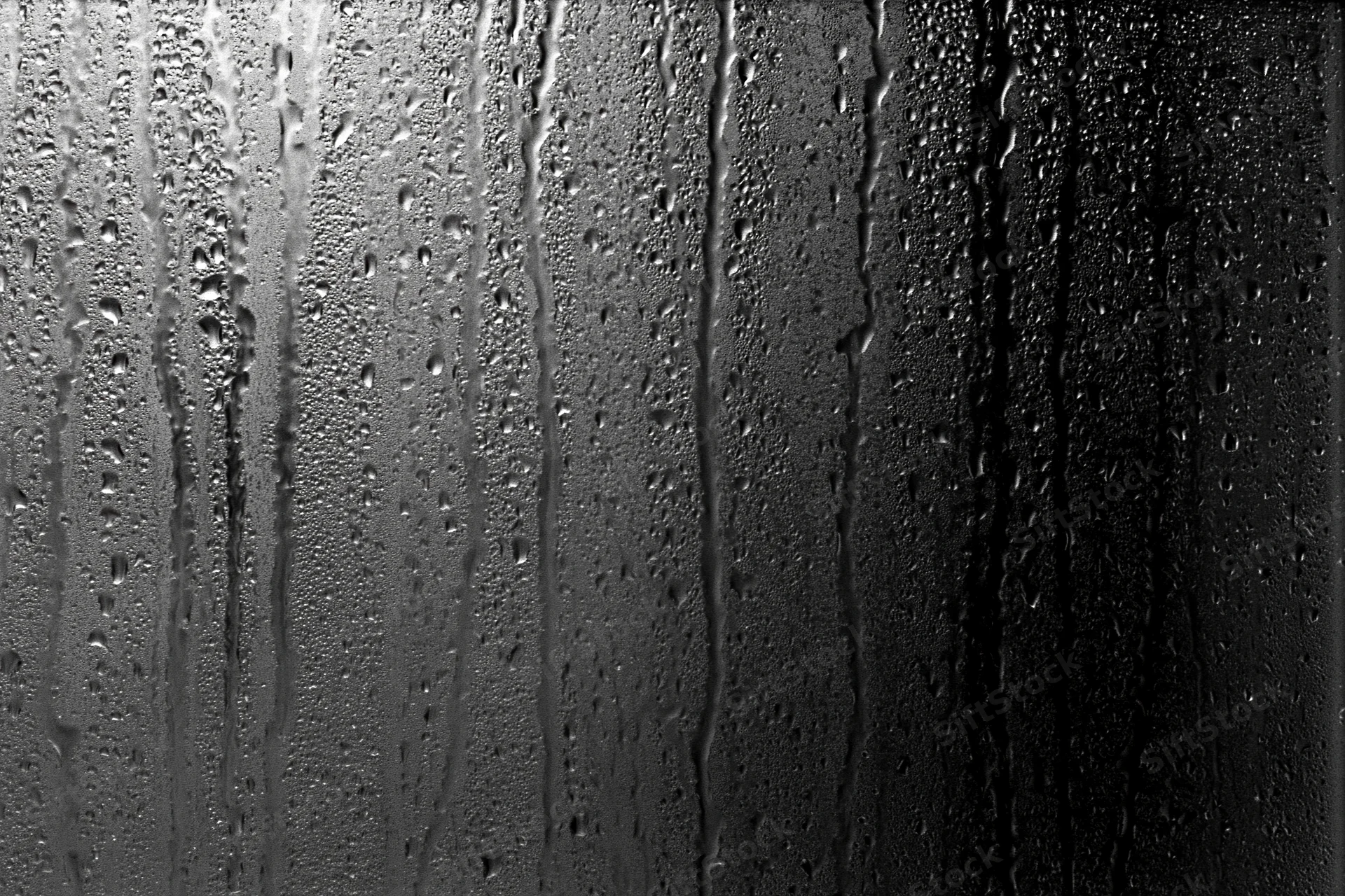 Rain-streaked dark glass window surface covered in water droplets and vertical streaks