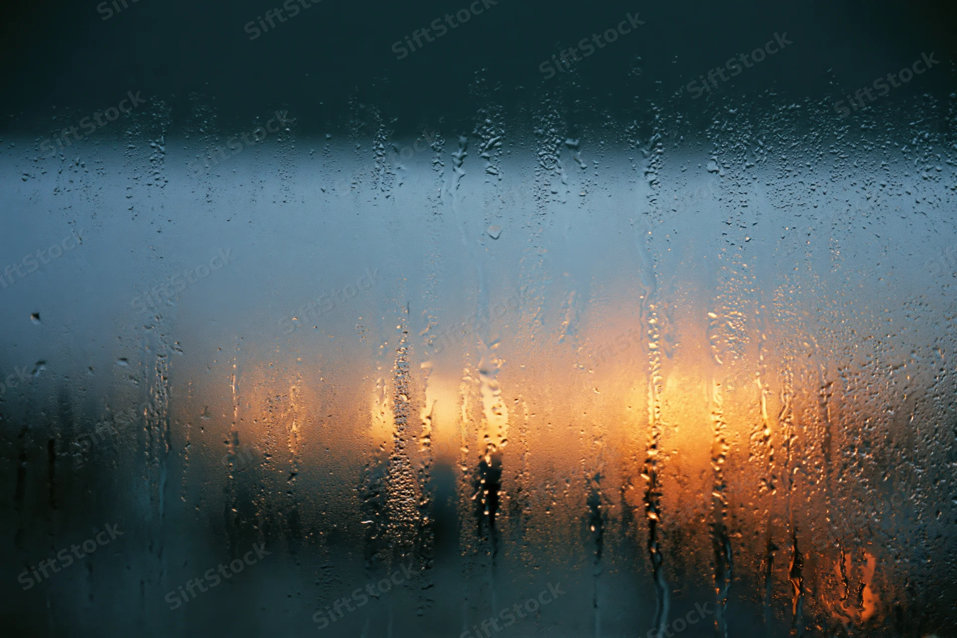 Rain-streaked window glass with condensation droplets and blurred city lights at twilight