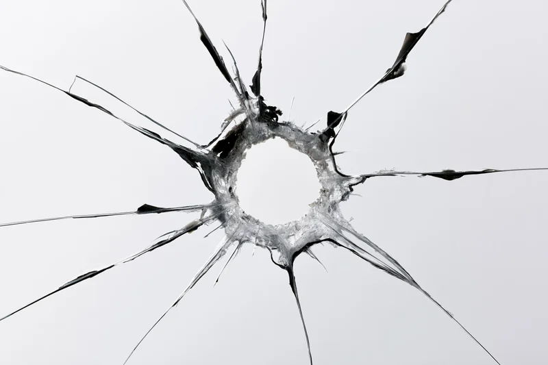 Close-up of a bullet hole in shattered glass with radial cracks radiating outward