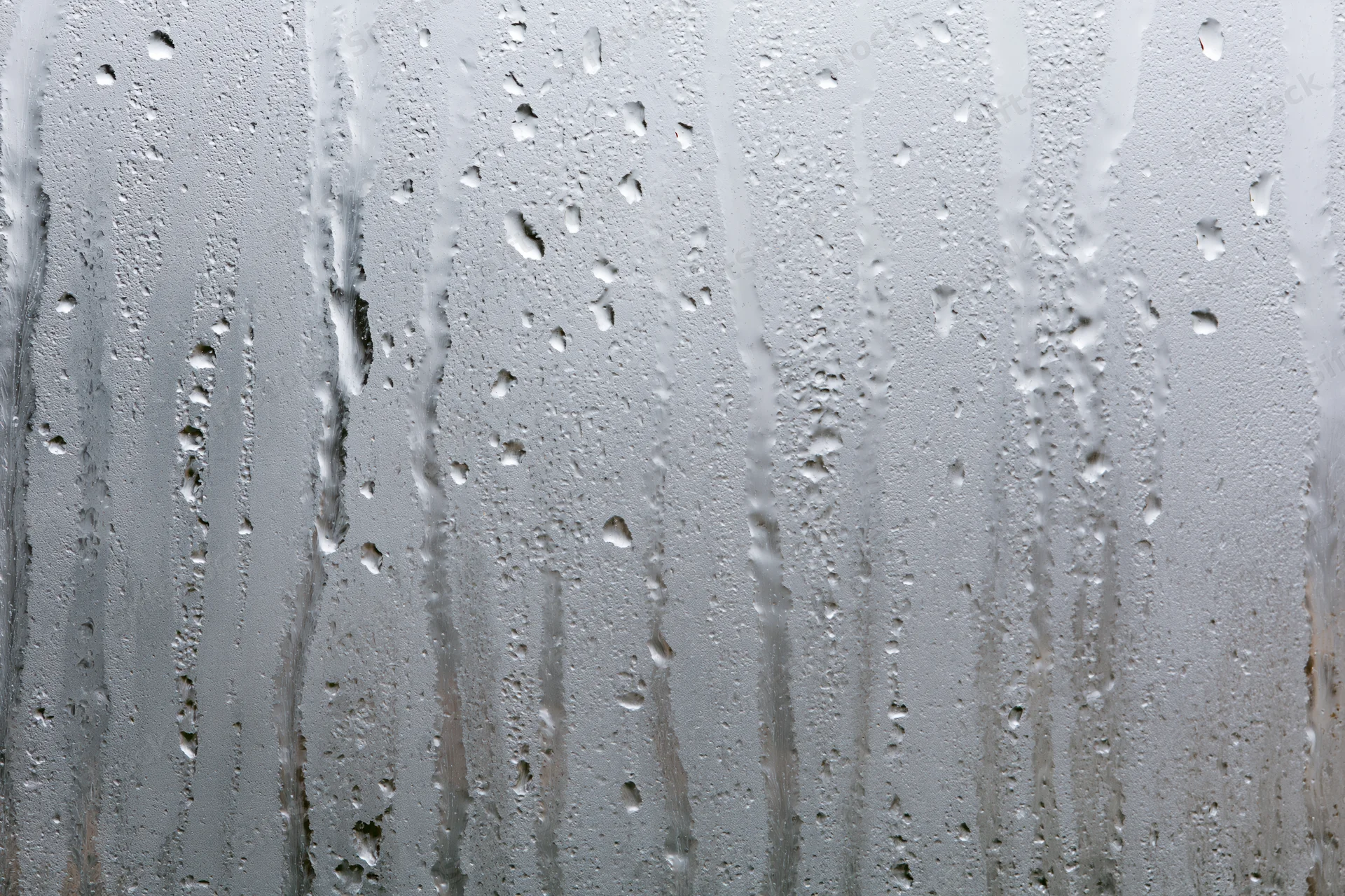 Close-up of condensation droplets and streaks on a wet glass window surface