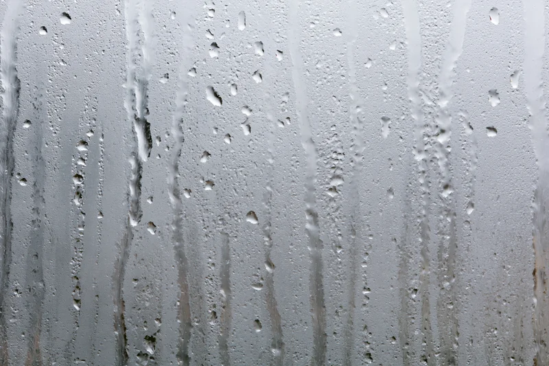 Close-up of condensation droplets and streaks on a wet glass window surface