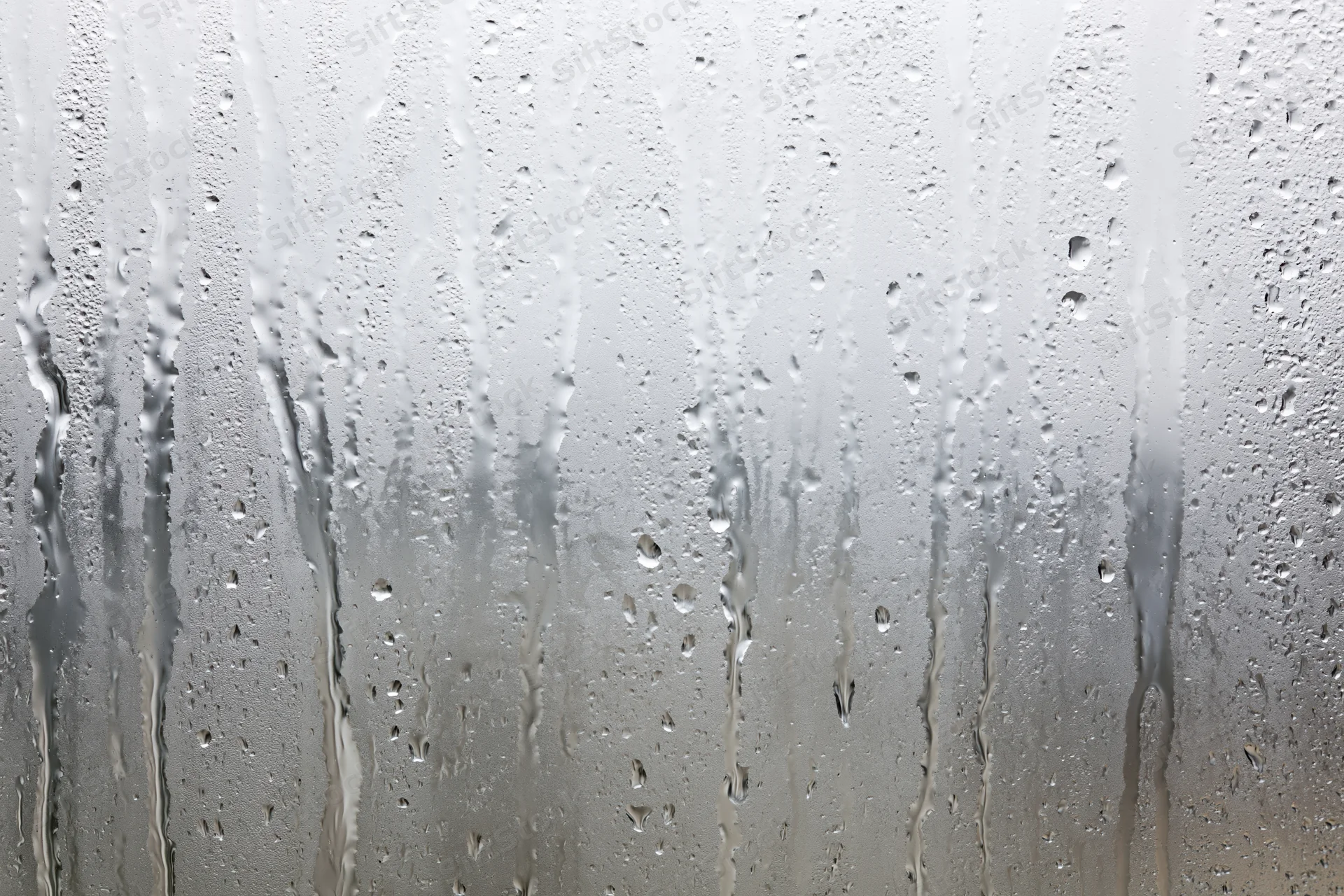Wet glass window covered in condensation and raindrops with streaks flowing down the surface
