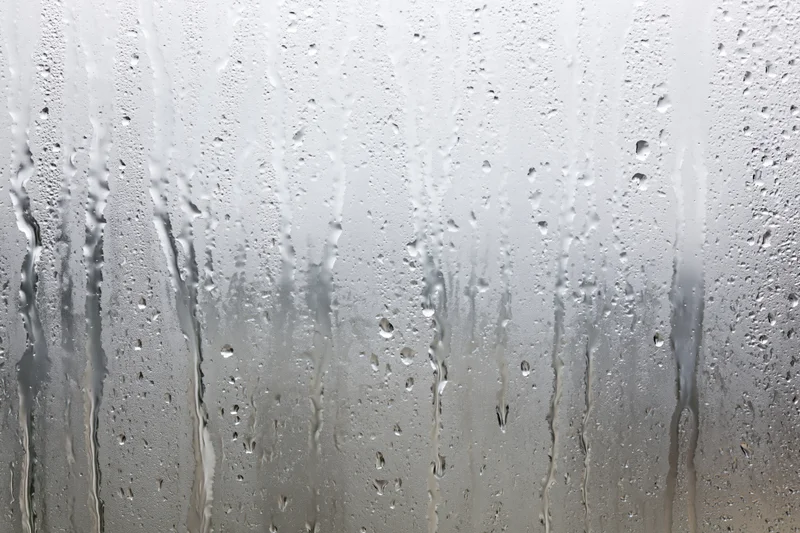 Wet glass window covered in condensation and raindrops with streaks flowing down the surface