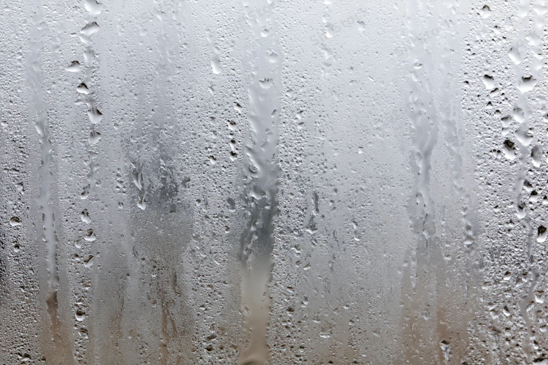 Close-up of condensation droplets and streaks on a wet glass window surface