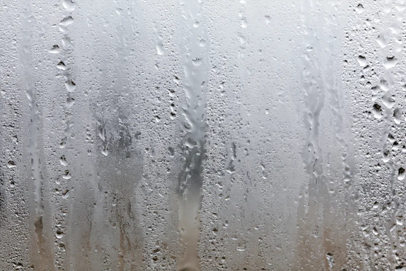 Close-up of condensation droplets and streaks on a wet glass window surface