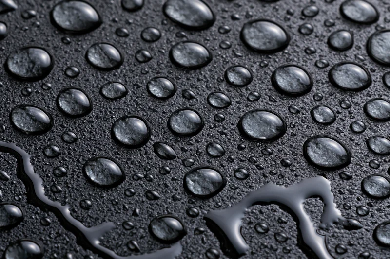Water droplets scattered across a dark wet glass surface