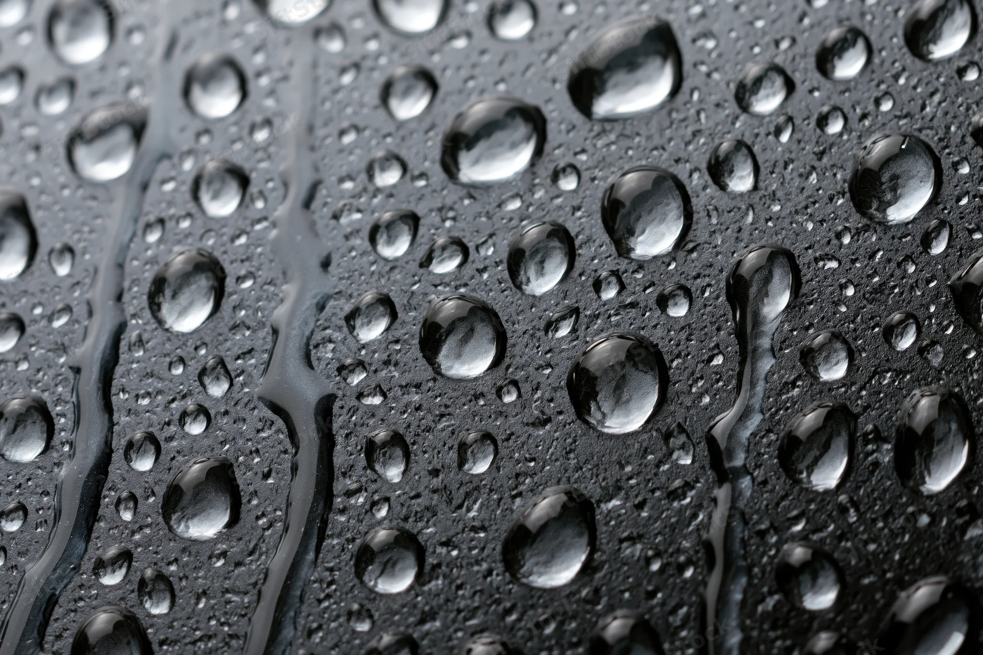 Water droplets scattered across dark wet glass surface