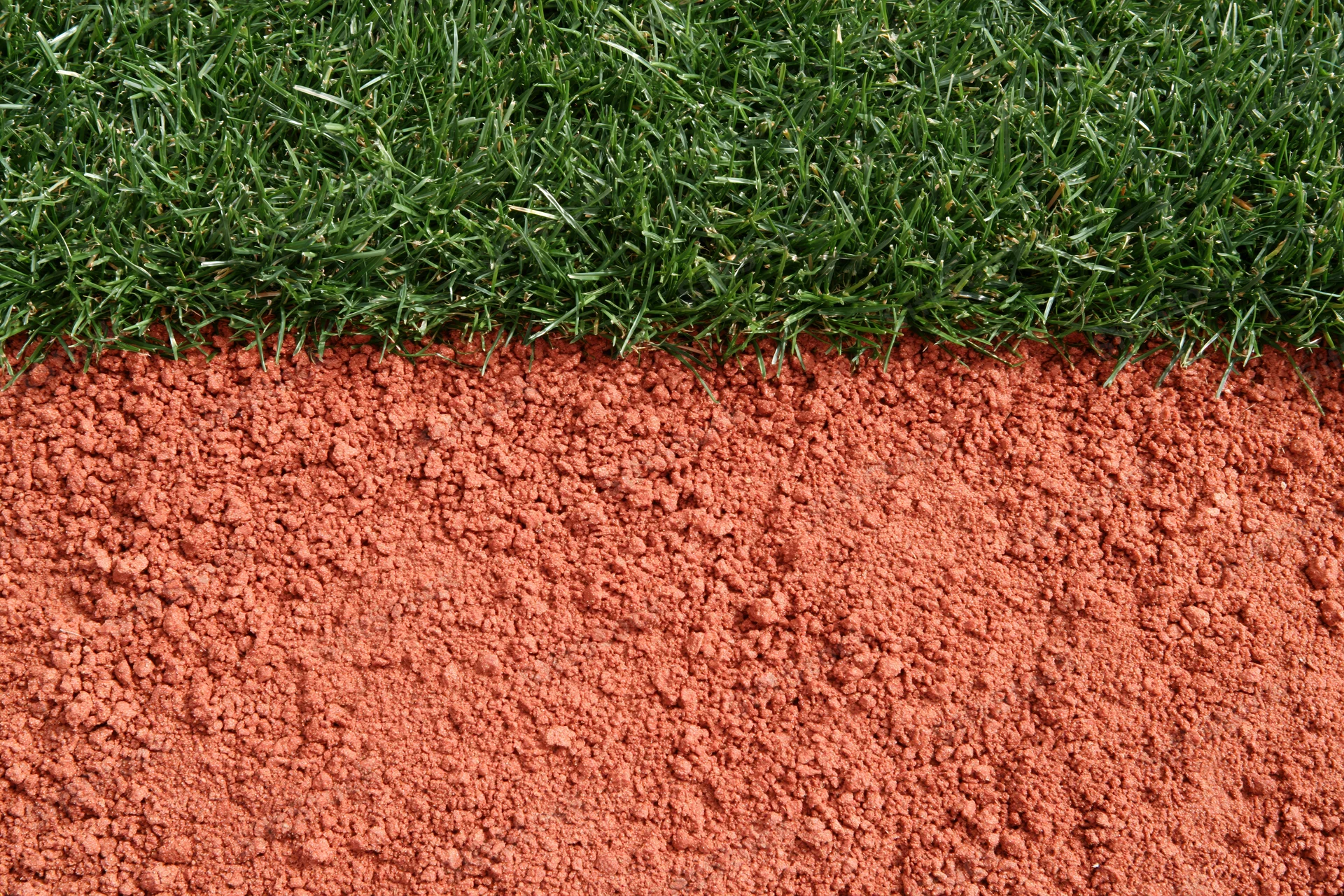Baseball field edge with red clay dirt and green grass border, overhead close-up view