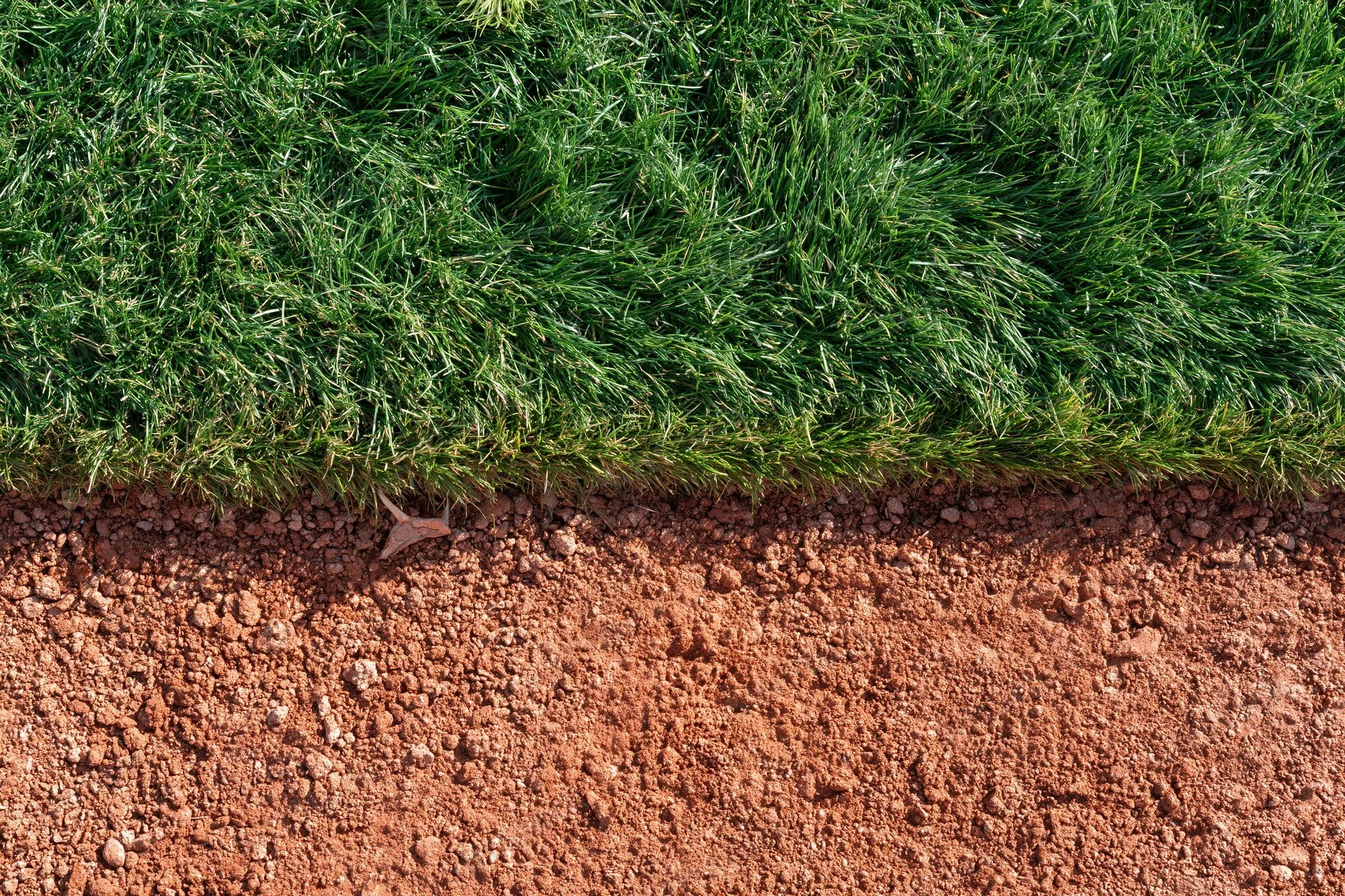 Close-up overhead view of baseball field edge showing green grass meeting red clay dirt