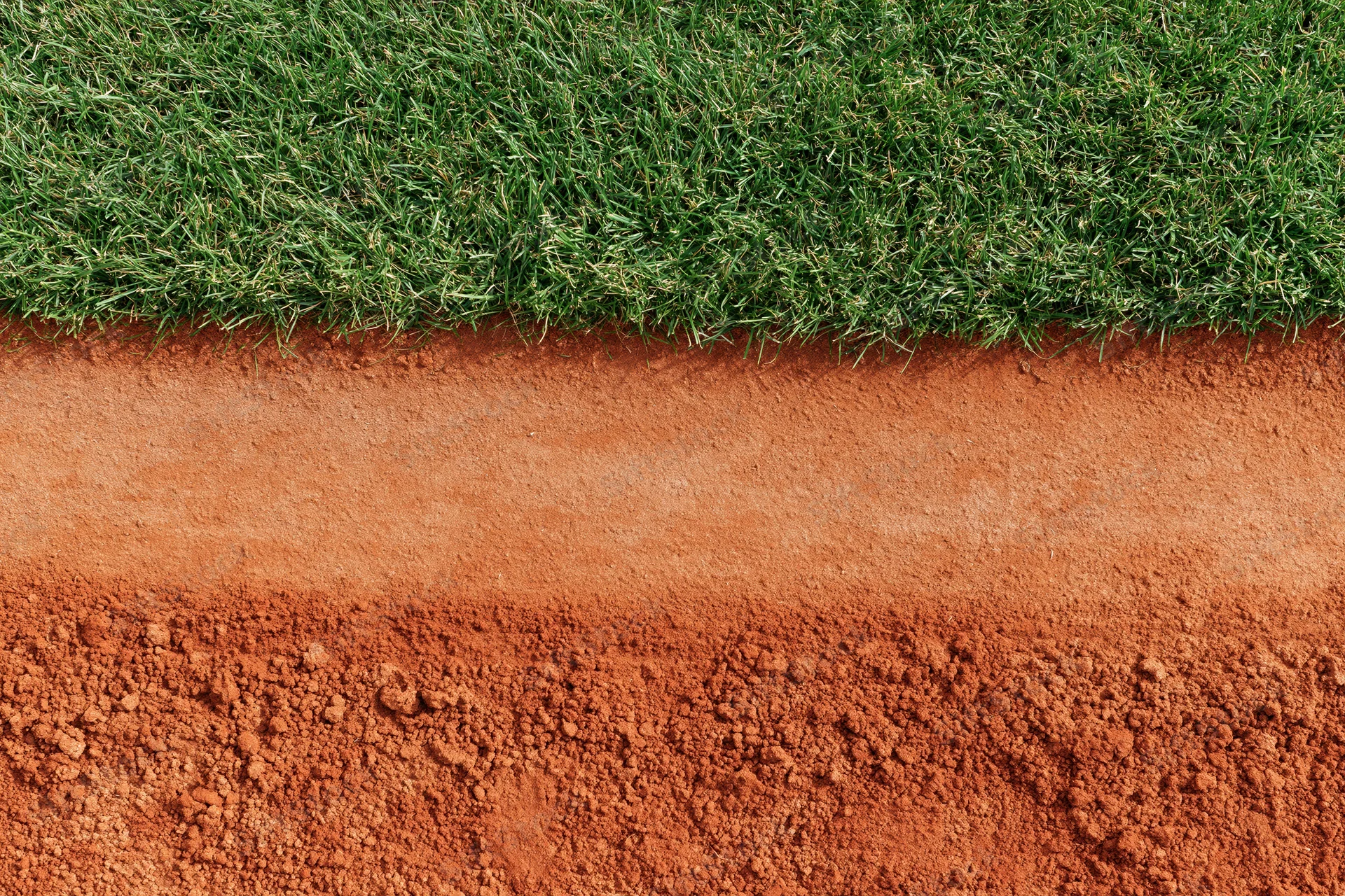 Close-up overhead view of baseball field edge showing red clay dirt and green grass boundary