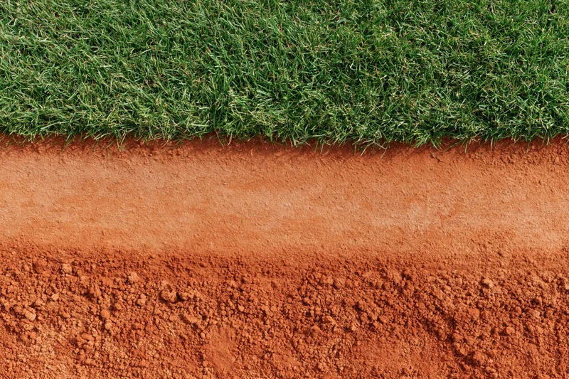 Close-up overhead view of baseball field edge showing red clay dirt and green grass boundary