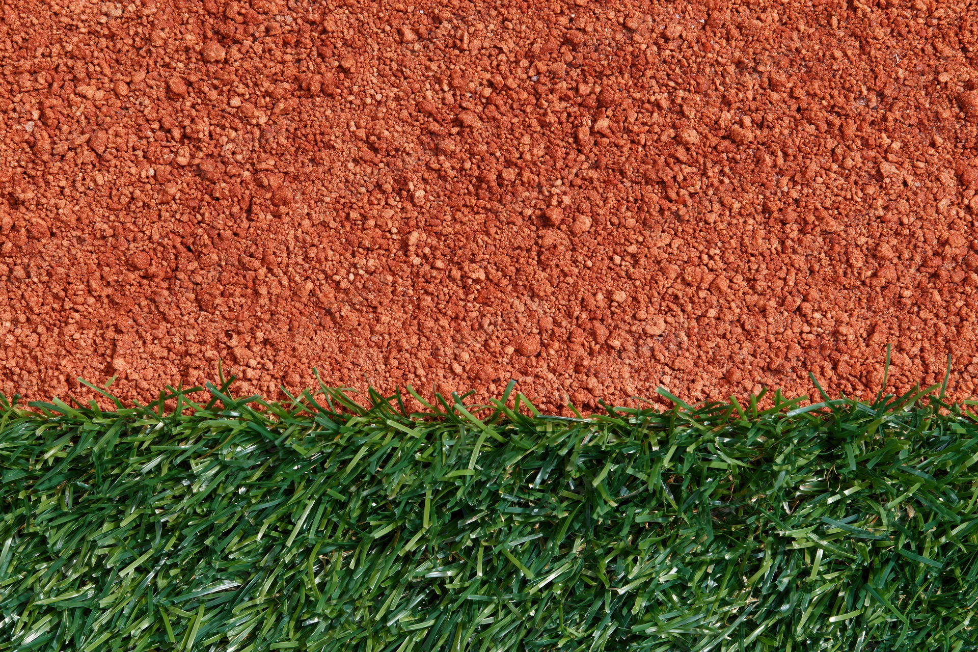 Close-up overhead view of baseball field edge with artificial green turf meeting red clay dirt