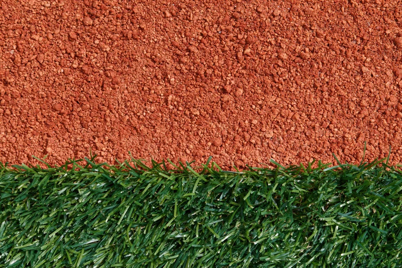 Close-up overhead view of baseball field edge with artificial green turf meeting red clay dirt