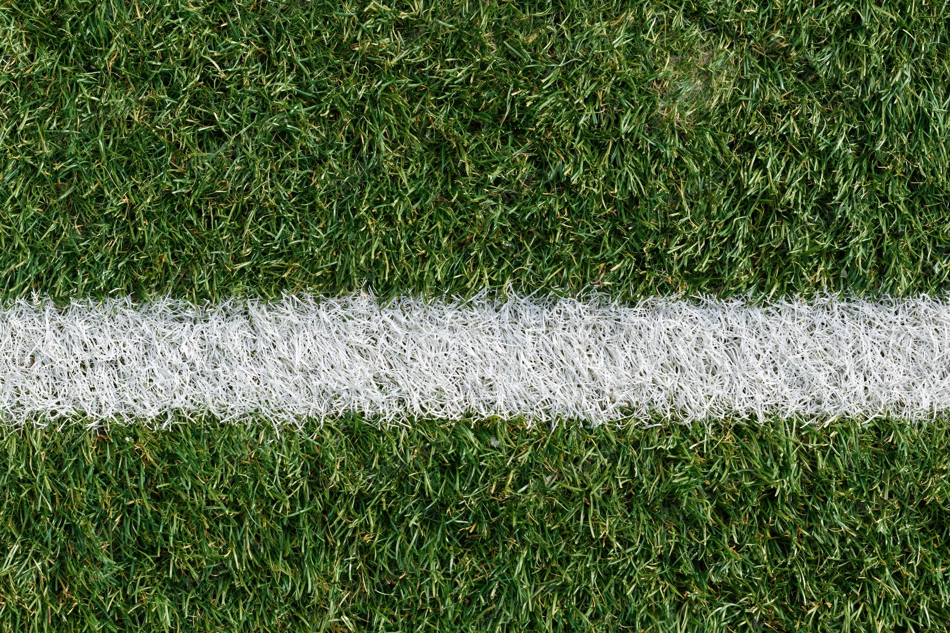 Close-up overhead view of artificial turf with white boundary line on sports field