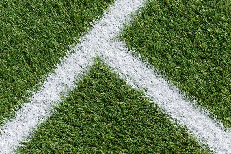 Close-up overhead view of artificial turf soccer field corner with white boundary line