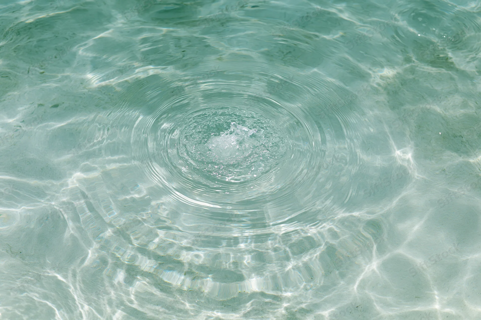 Circular ripples spreading across shallow clear pool water surface under sunlight