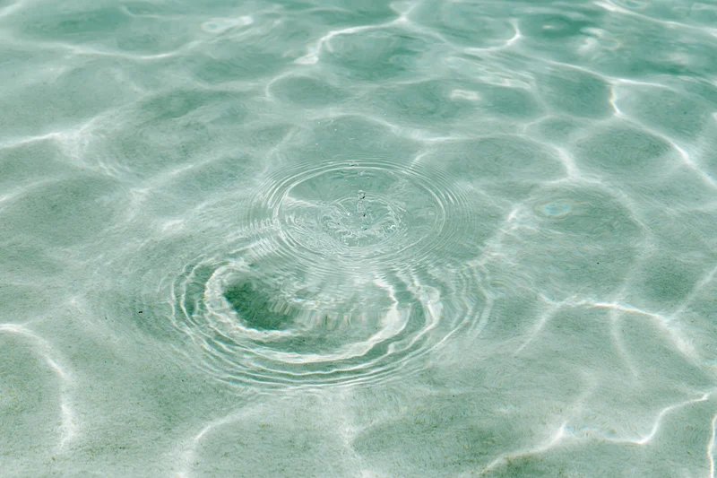 Ripples spreading across shallow pool water surface under sunlight