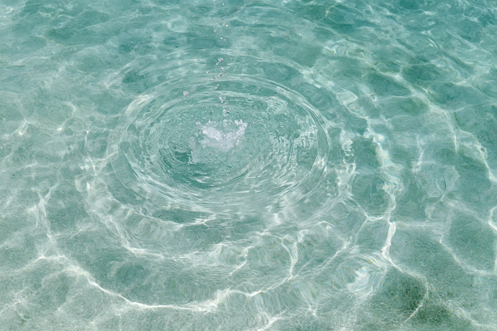 Shallow pool water surface with circular ripples spreading outward from a central splash