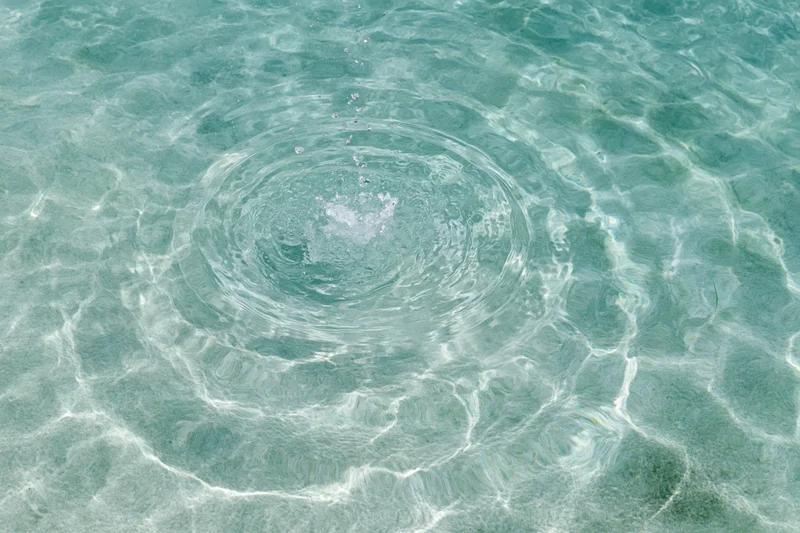 Shallow pool water surface with circular ripples spreading outward from a central splash