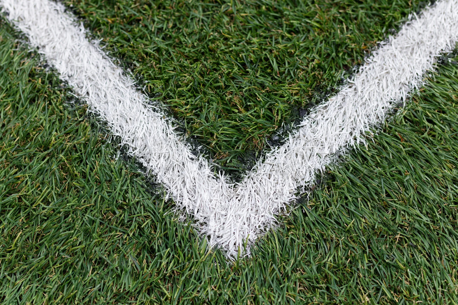 Close-up top-down view of white corner marking lines on green soccer field turf
