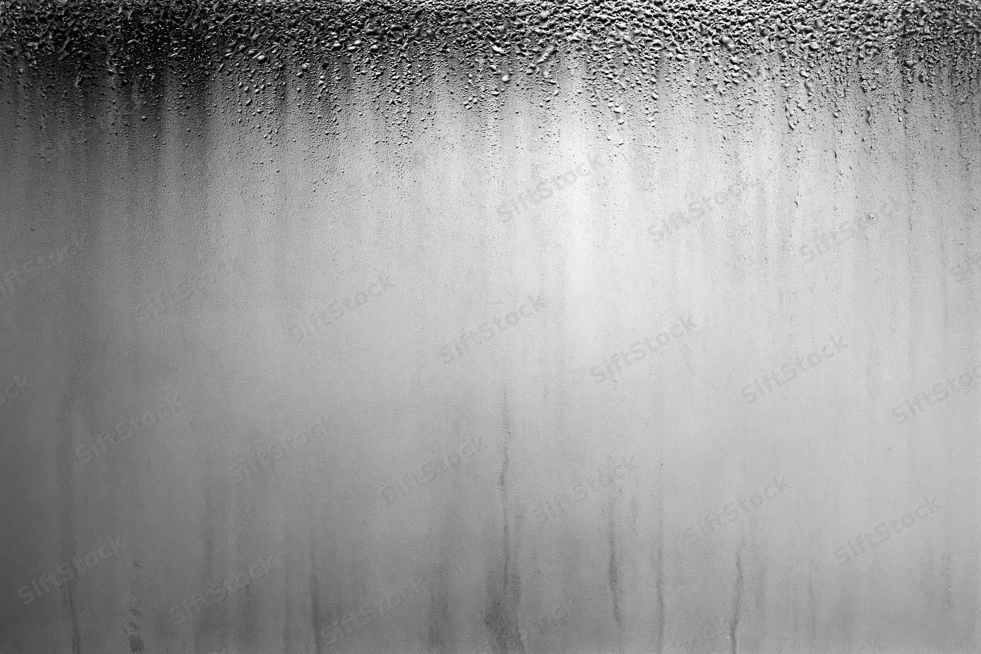 Condensation droplets and water streaks running down a fogged glass surface